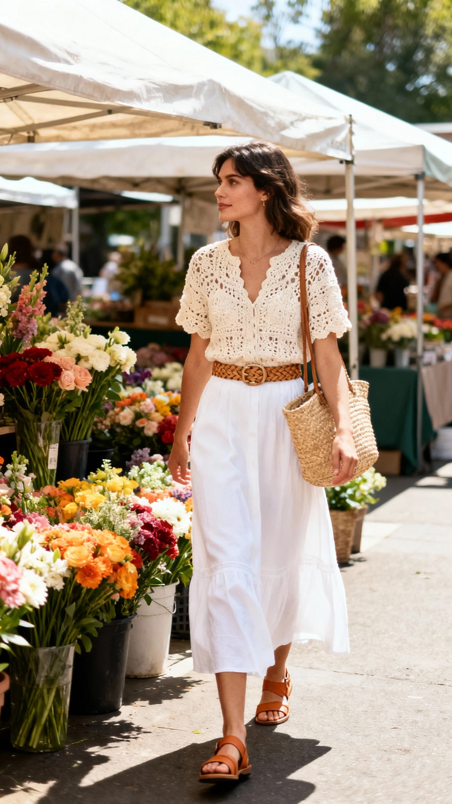 Natural lifestyle photo of a woman wearing a white maxi skirt with a cream crochet top, woven belt, straw tote, and tan sandals, strolling through a weekend market with flowers, face looking away, sunny daylight, iPhone photo quality.