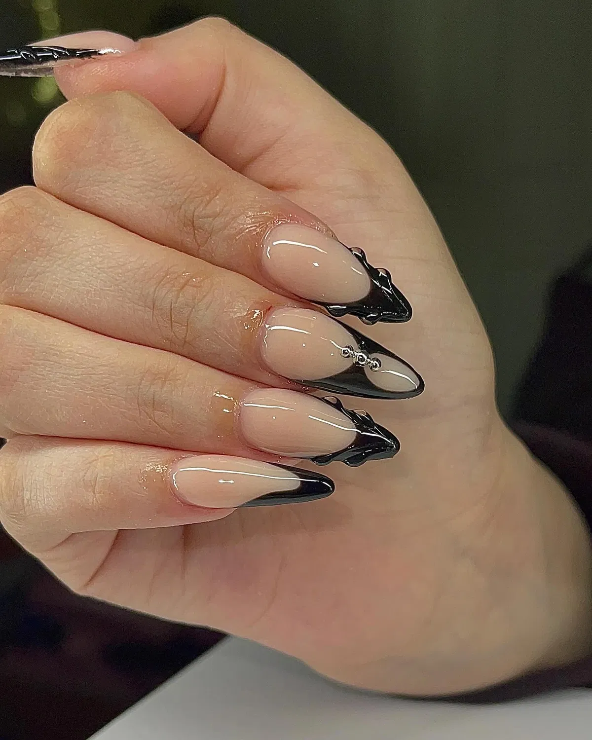Nude almond nails with sharp black V-tips and bead accent