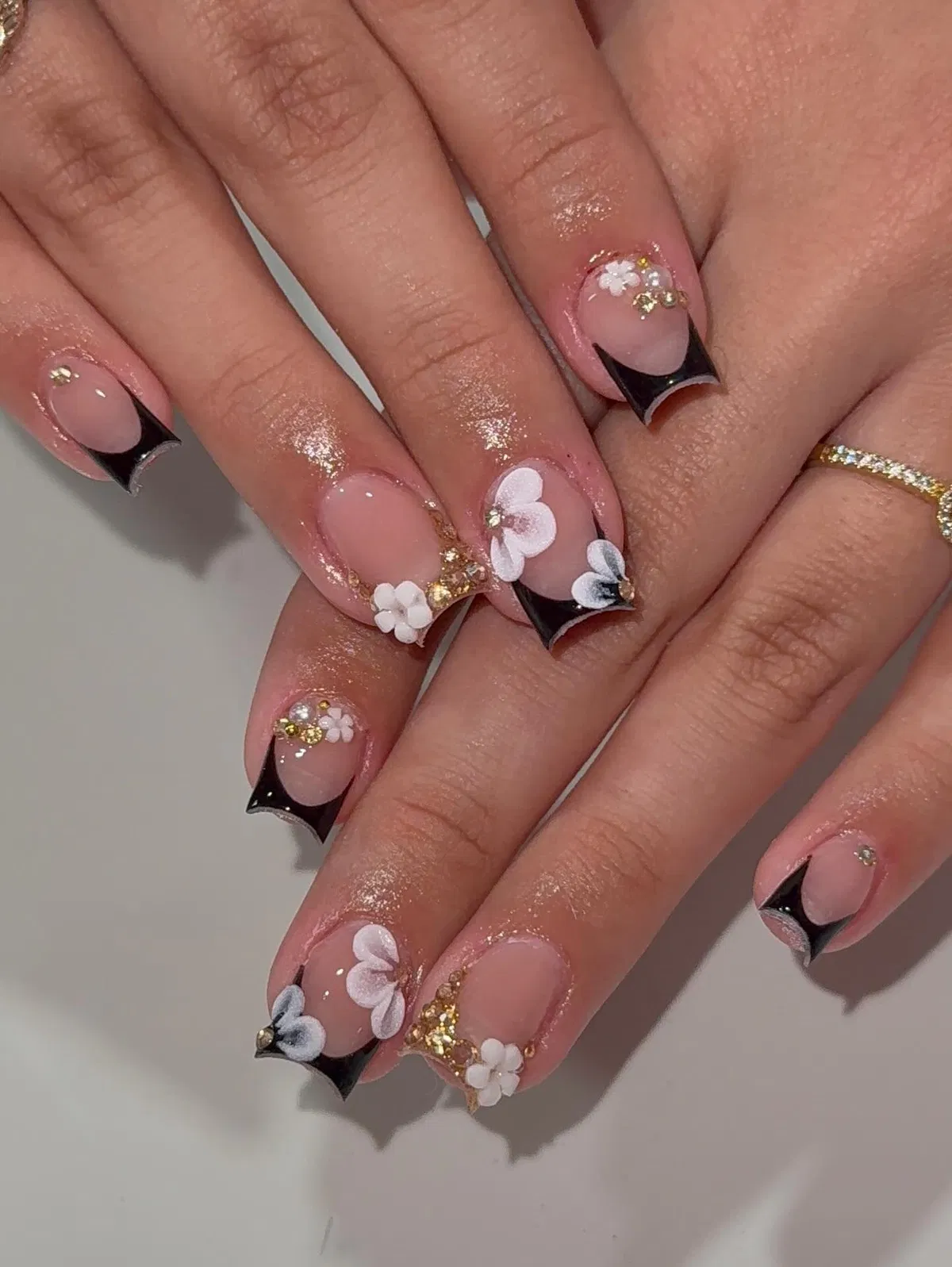 Black curved French tips with white flowers and gold glitter