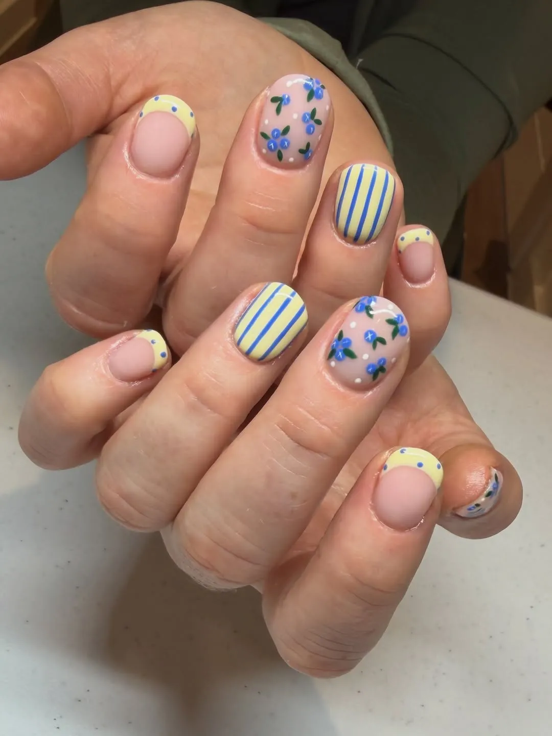 Short nails with yellow tips, stripes, and blue florals