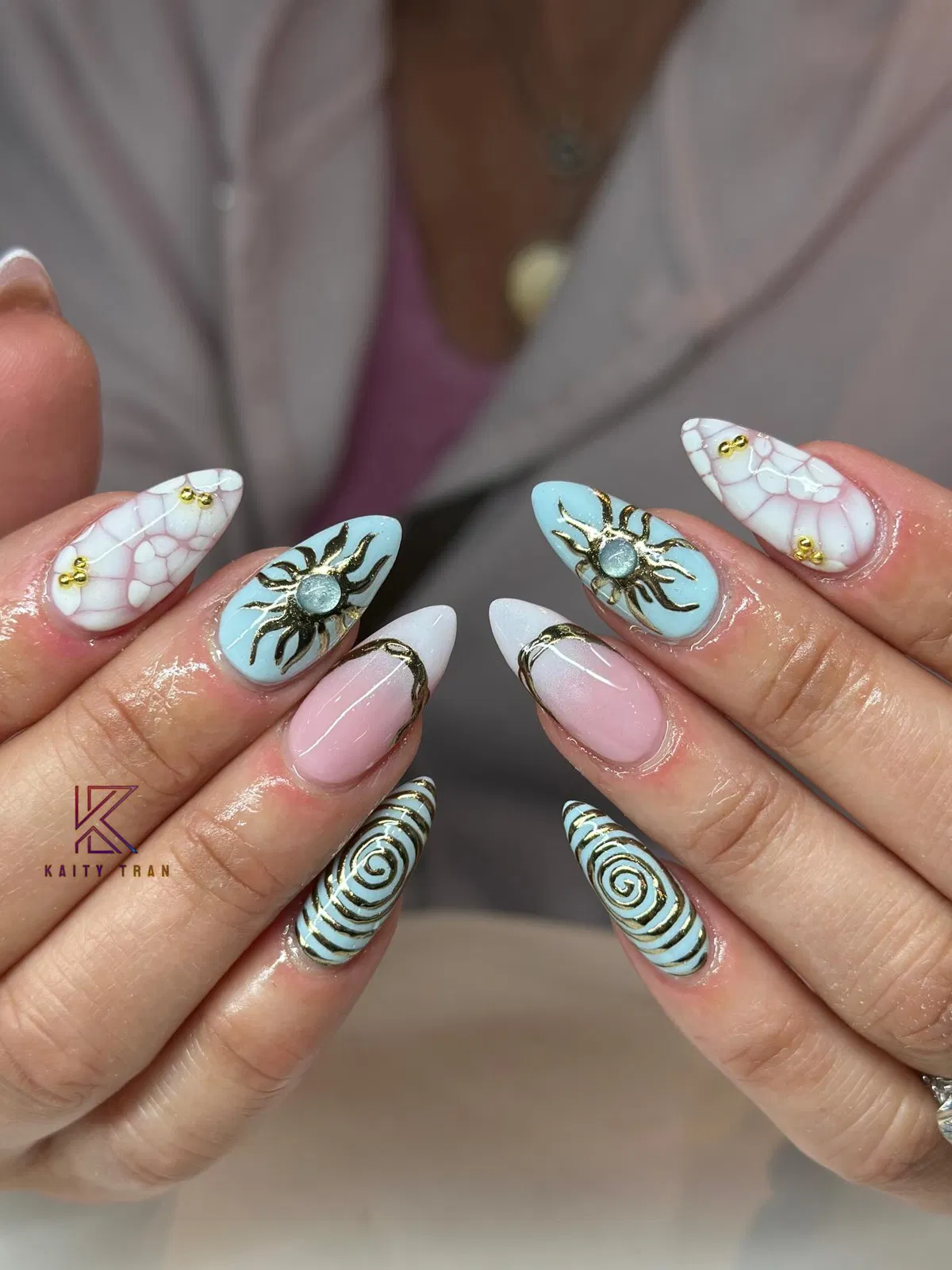 Pastel blue/pink nails with gold sun and spiral details