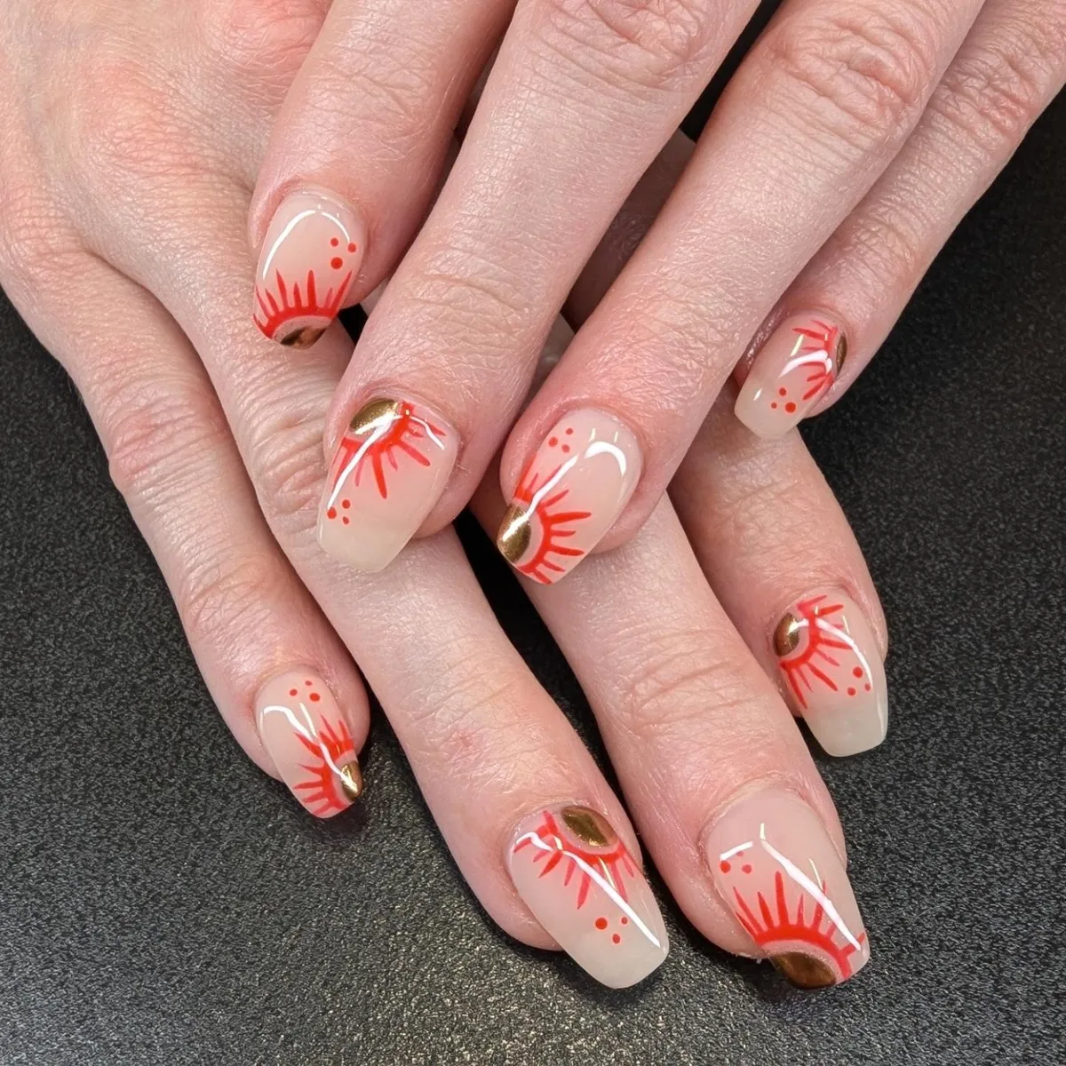Nude nails with red sunburst lines and gold accents