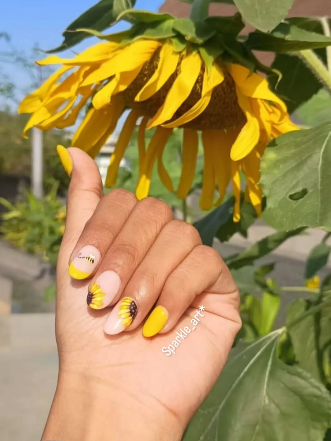 Short nude nails with yellow tips, floral accents, and a bee detail
