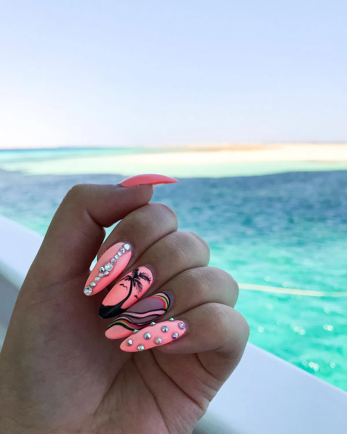 Coral-pink almond nails with rhinestones and palm silhouette