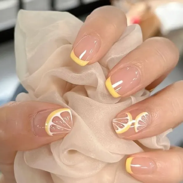 Almond nude nails with thin yellow tips and lemon slices
