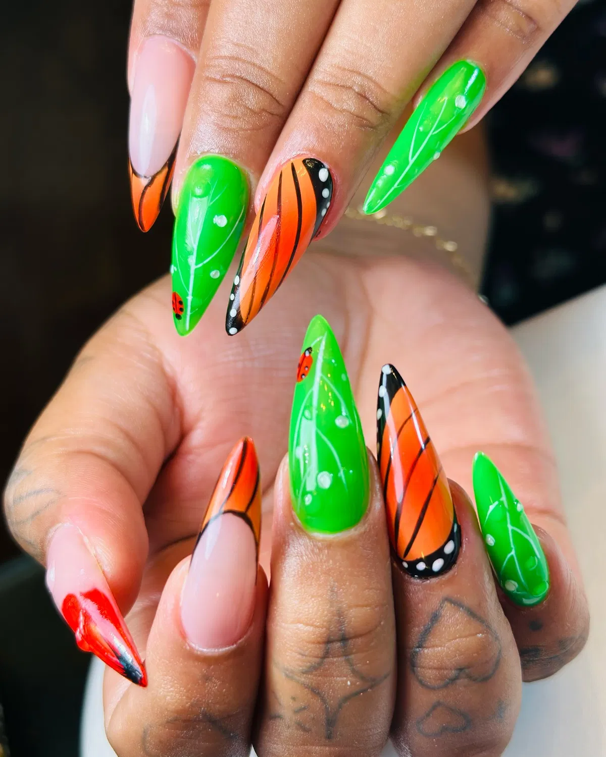 Bright green and orange graphic nails with ladybug accents
