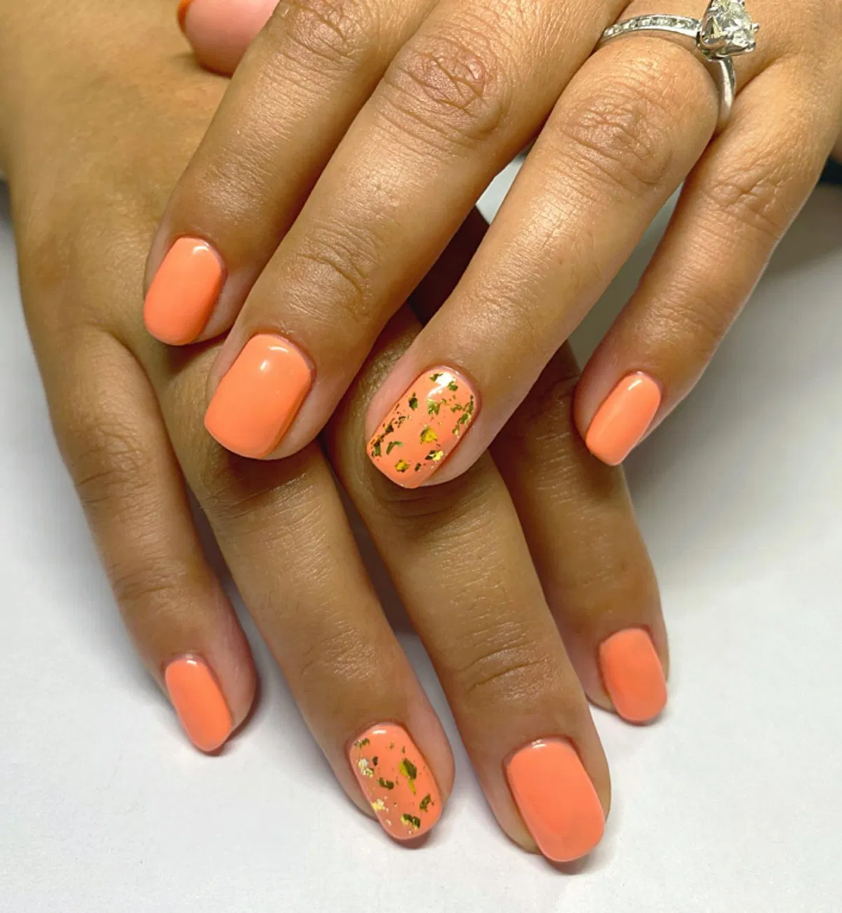 Peach-orange glossy nails with gold-fleck accents