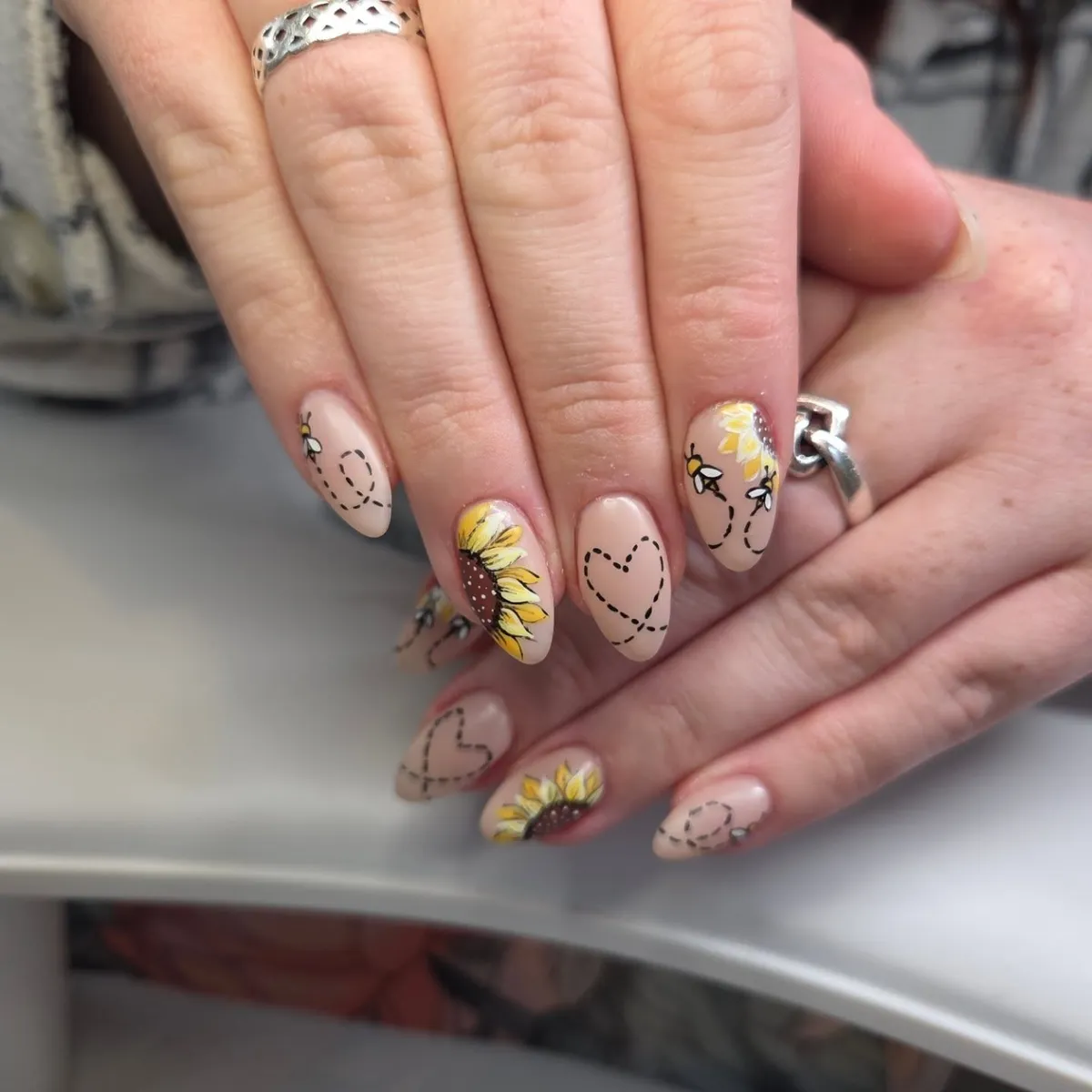 Bee-and-heart line art with sunflower accent on nude base