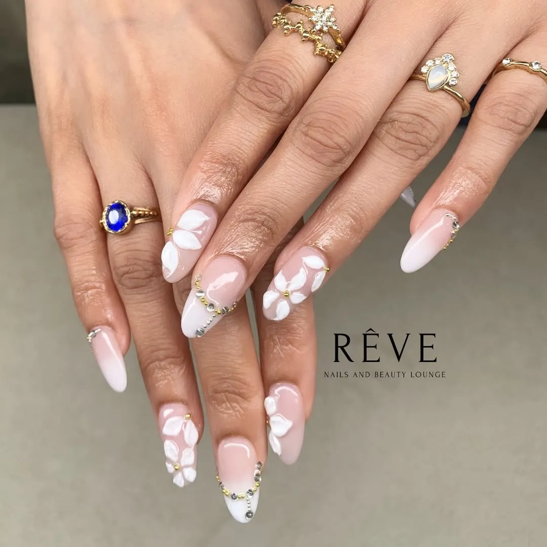 Pale pink long nails with raised white florals and rhinestone/bead edging