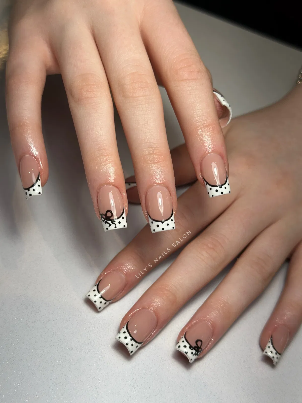 Square nude nails with dotted white French tips and bow details