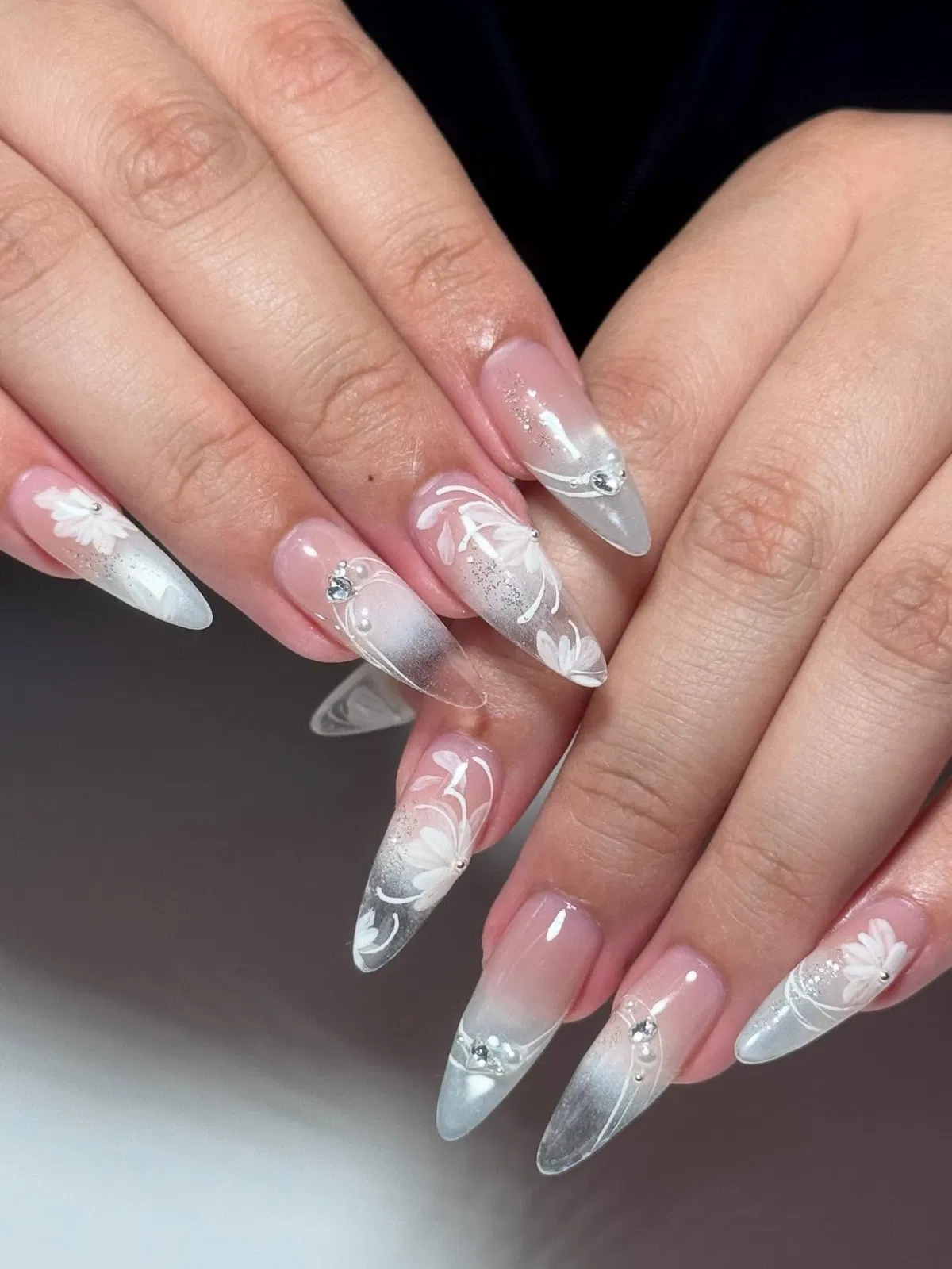 Sheer pink stiletto nails with translucent tips and white floral line art