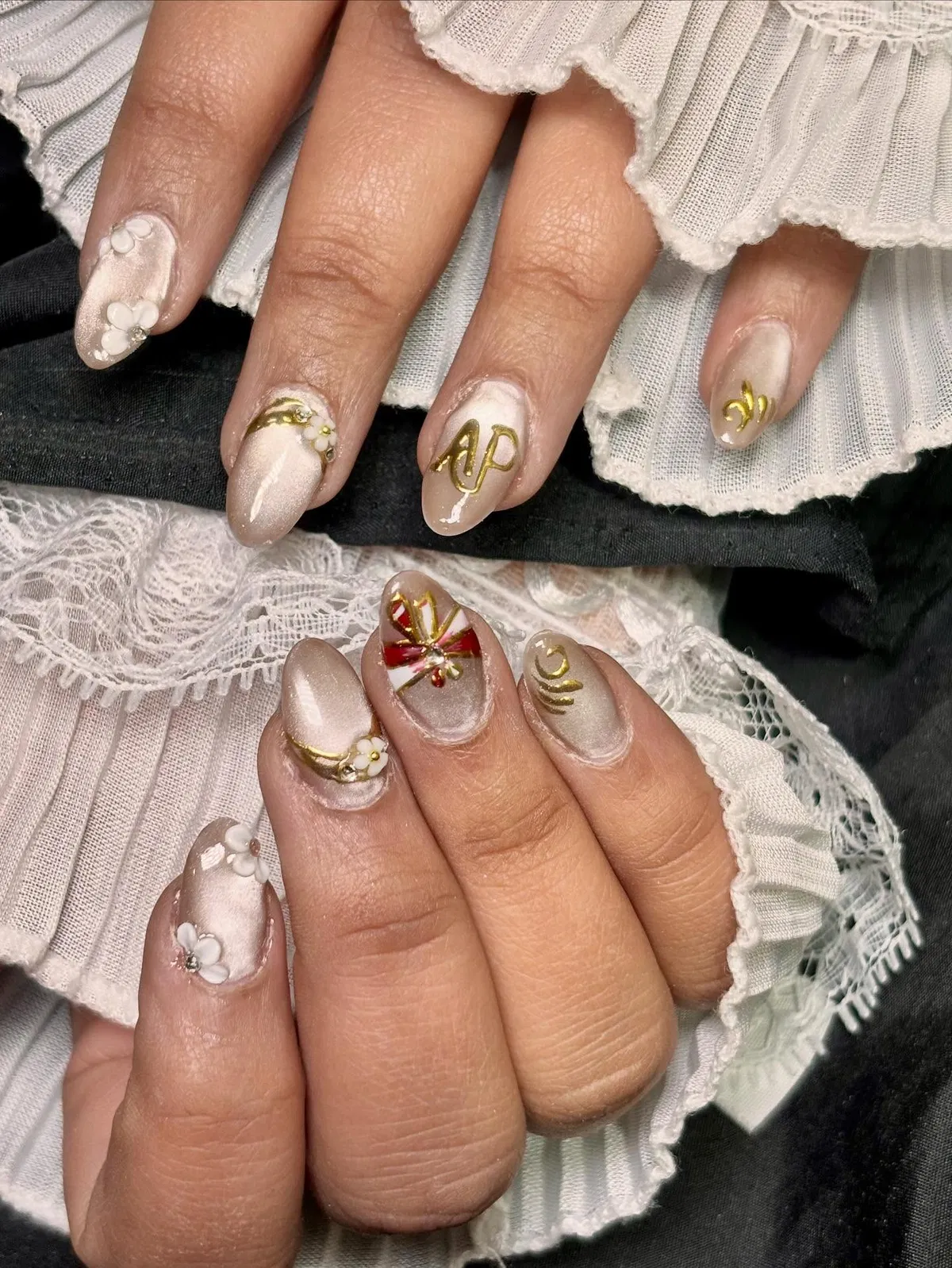 Pearly neutral nails with raised gold details and a red bow accent