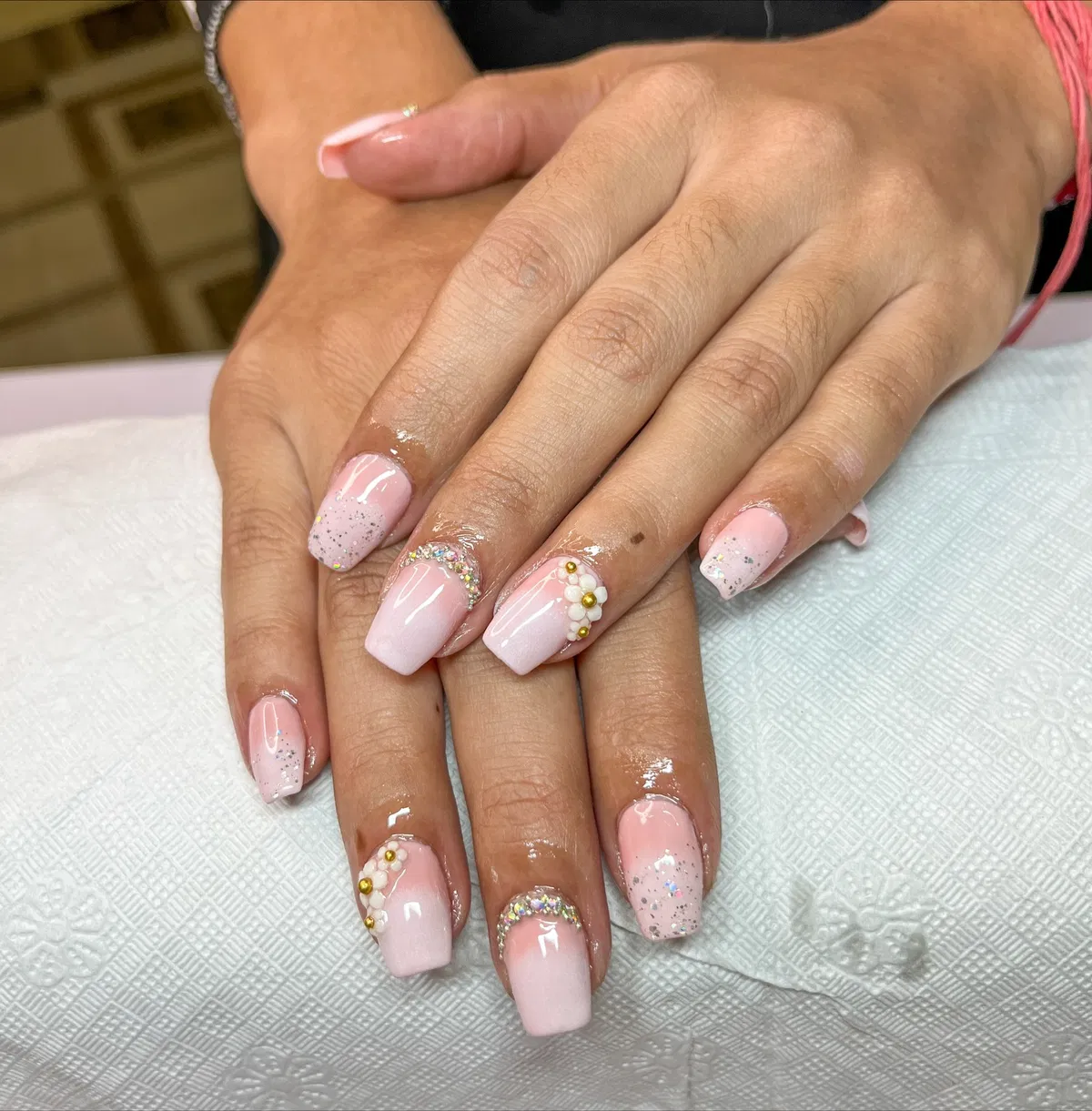 Light pink square nails with glitter, rhinestone arc, and floral cluster