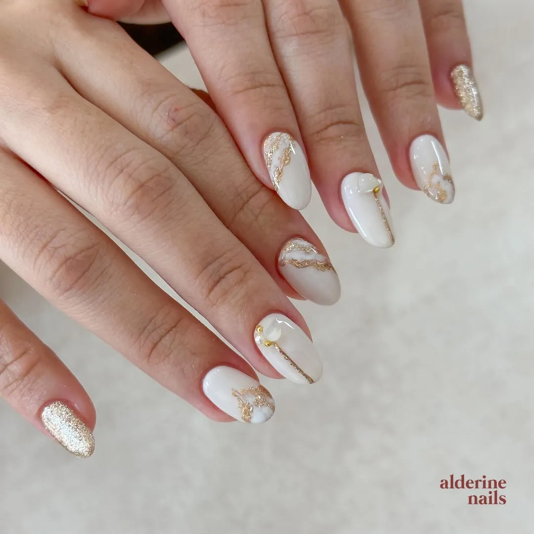 White and milky nude nails with gold veining and glitter accent