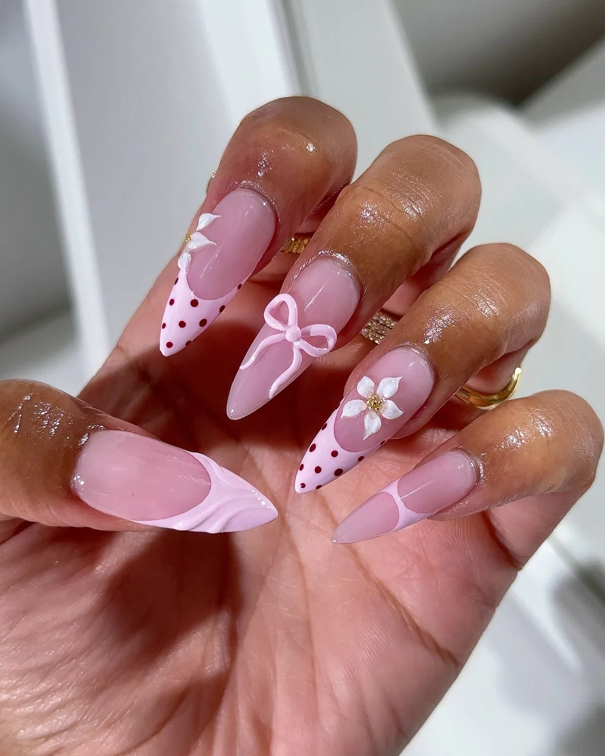 Stiletto pink nails with polka-dot tips and raised bow/flower accents