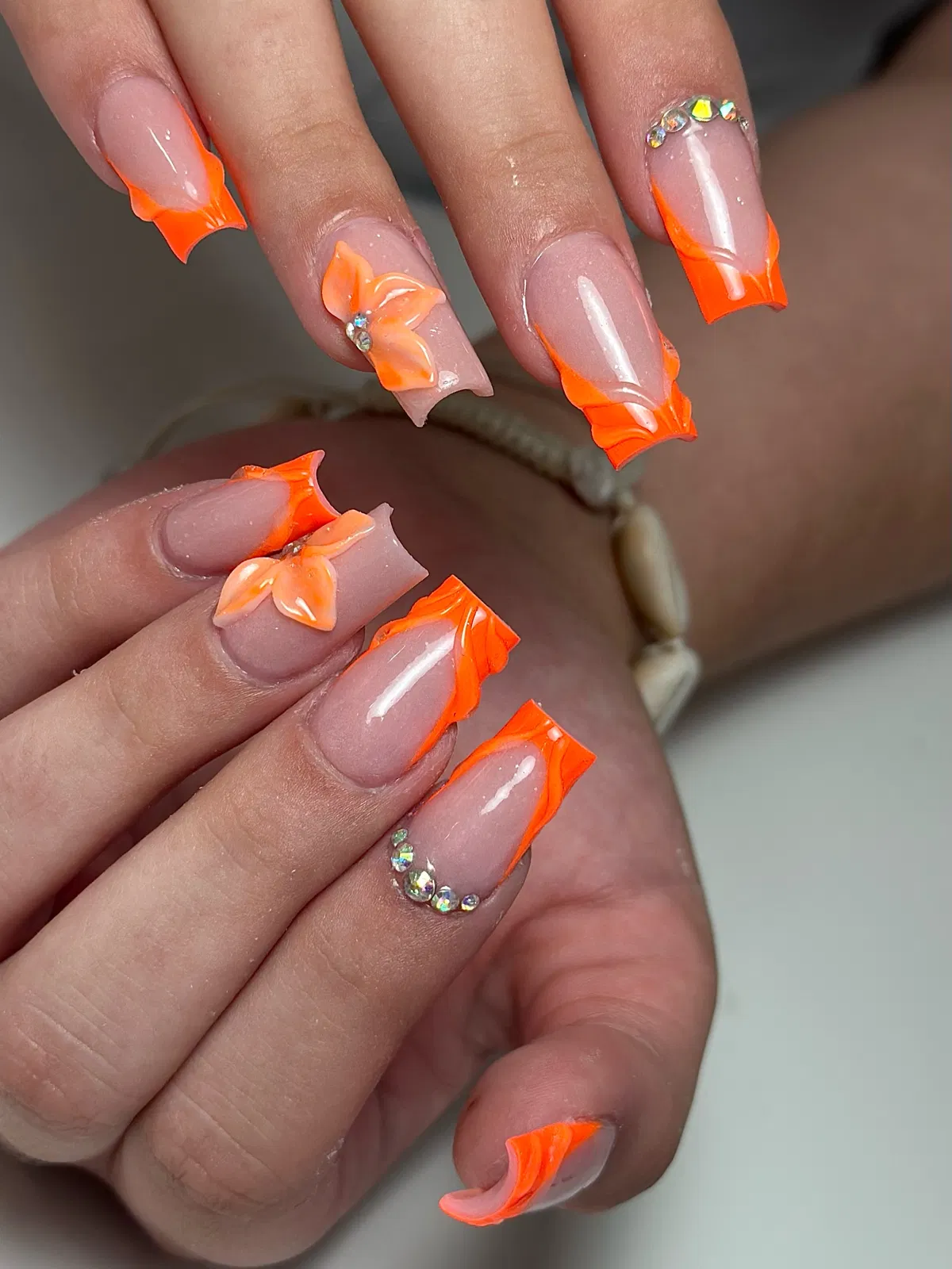 Wavy-edged orange French tips with 3D flower and rhinestones