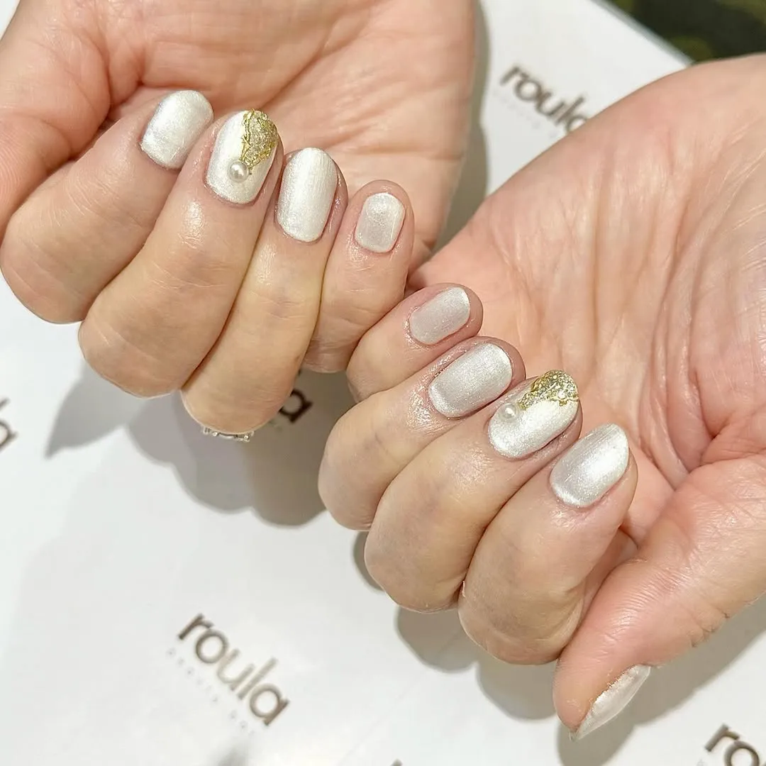Shimmery white nails with gold foil and pearl accents