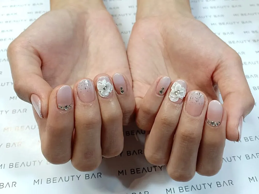 Muted nude-pink nails with raised white flowers and small rhinestone accents