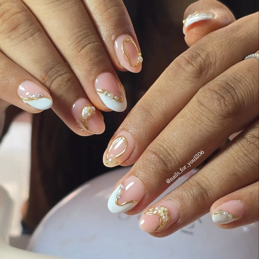 Short French tips with gold curves, rhinestones, and pearl-like accents