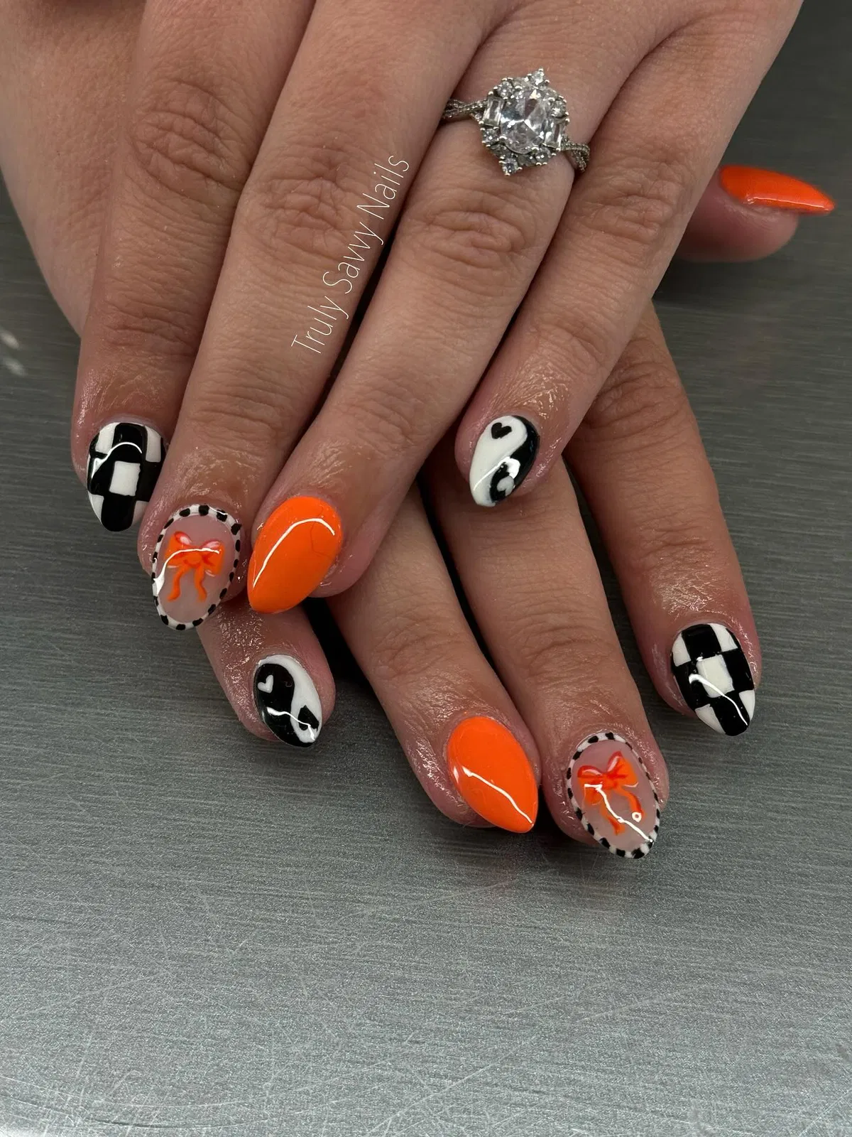 Bright orange accents with checkerboard, hearts, and bow nail art