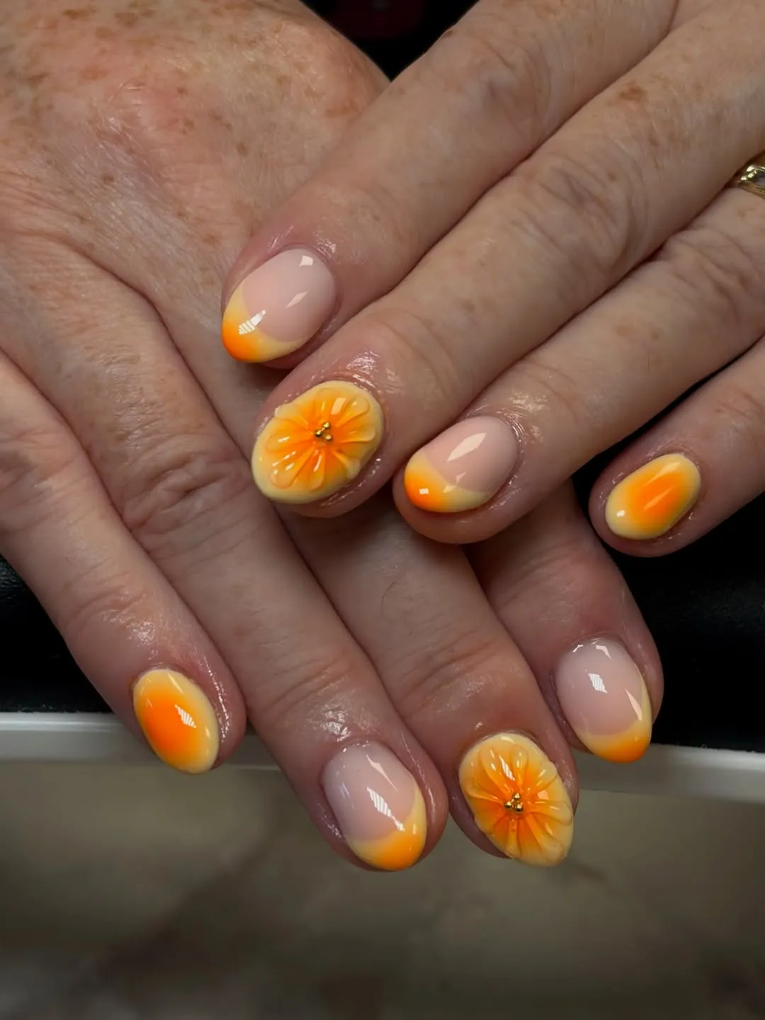 Soft nude base with orange ombrรฉ tips and raised flowers