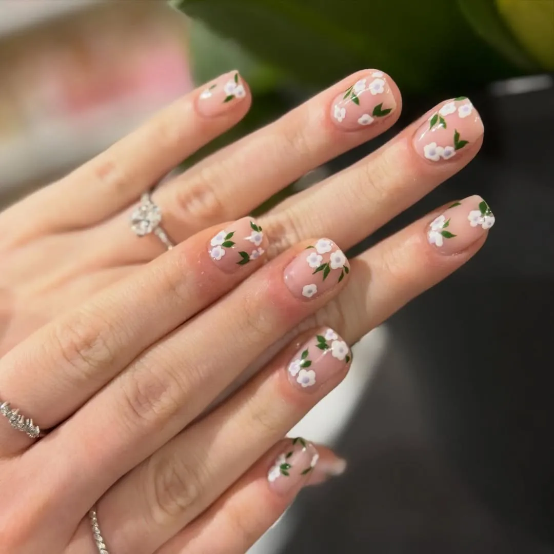 Nude-pink short nails with white flowers and green leaves