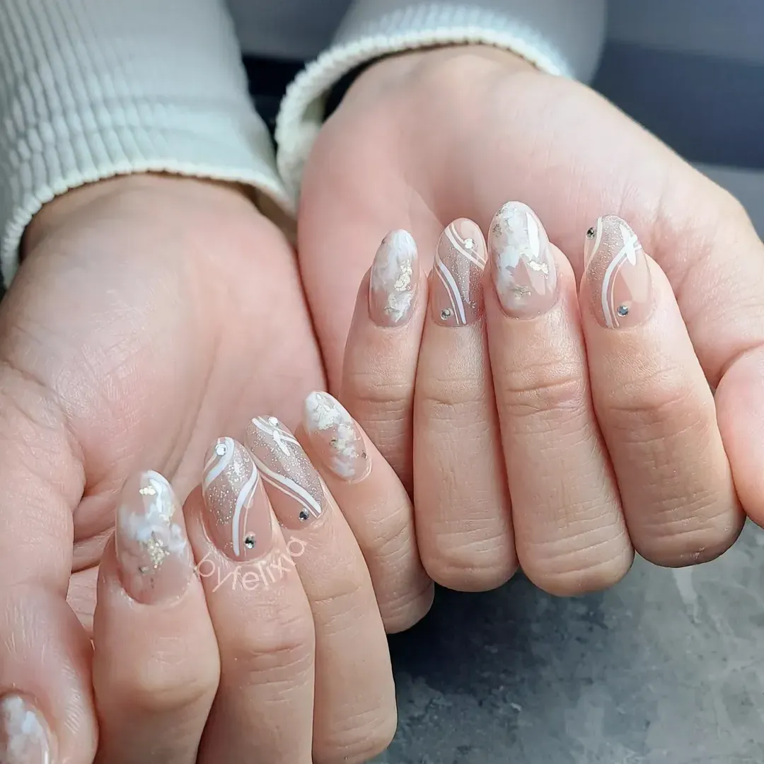 Nude almond nails with white wavy lines, cloud-like accents, and rhinestones
