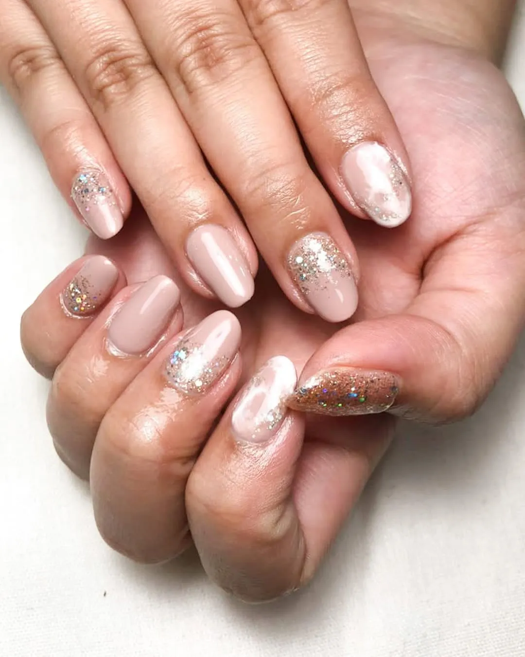 Glossy nude-pink nails with silver glitter accents