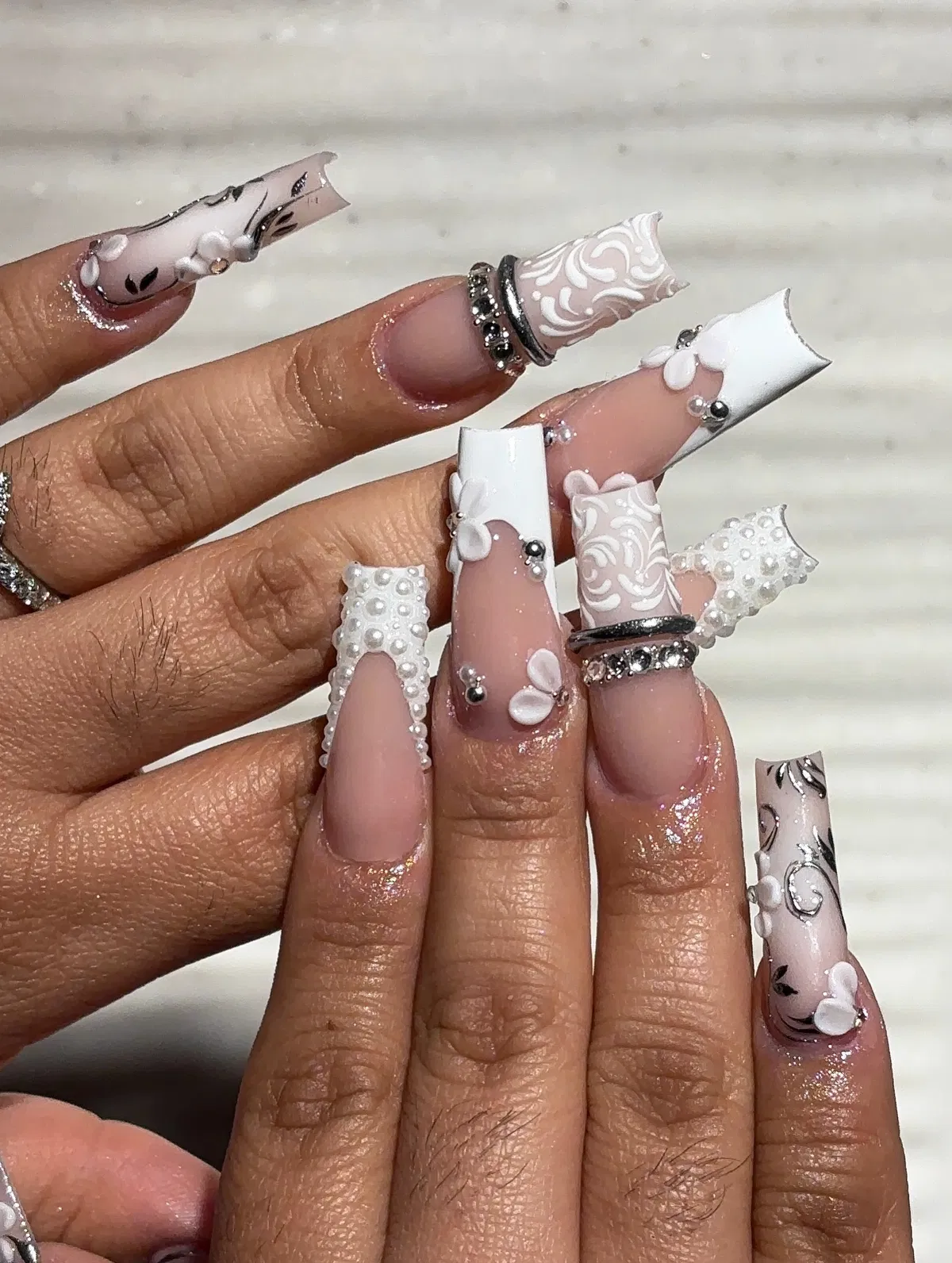Extra-long square nails with pearl-like beads, rhinestone-like sparkle, and raised white swirls