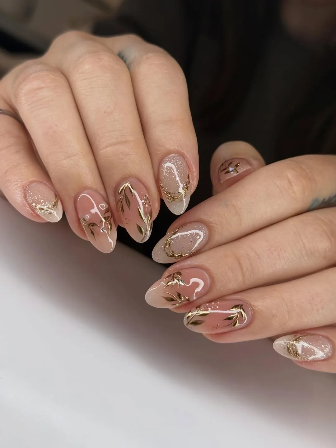 Nude almond nails with gold vine motifs and glitter accents