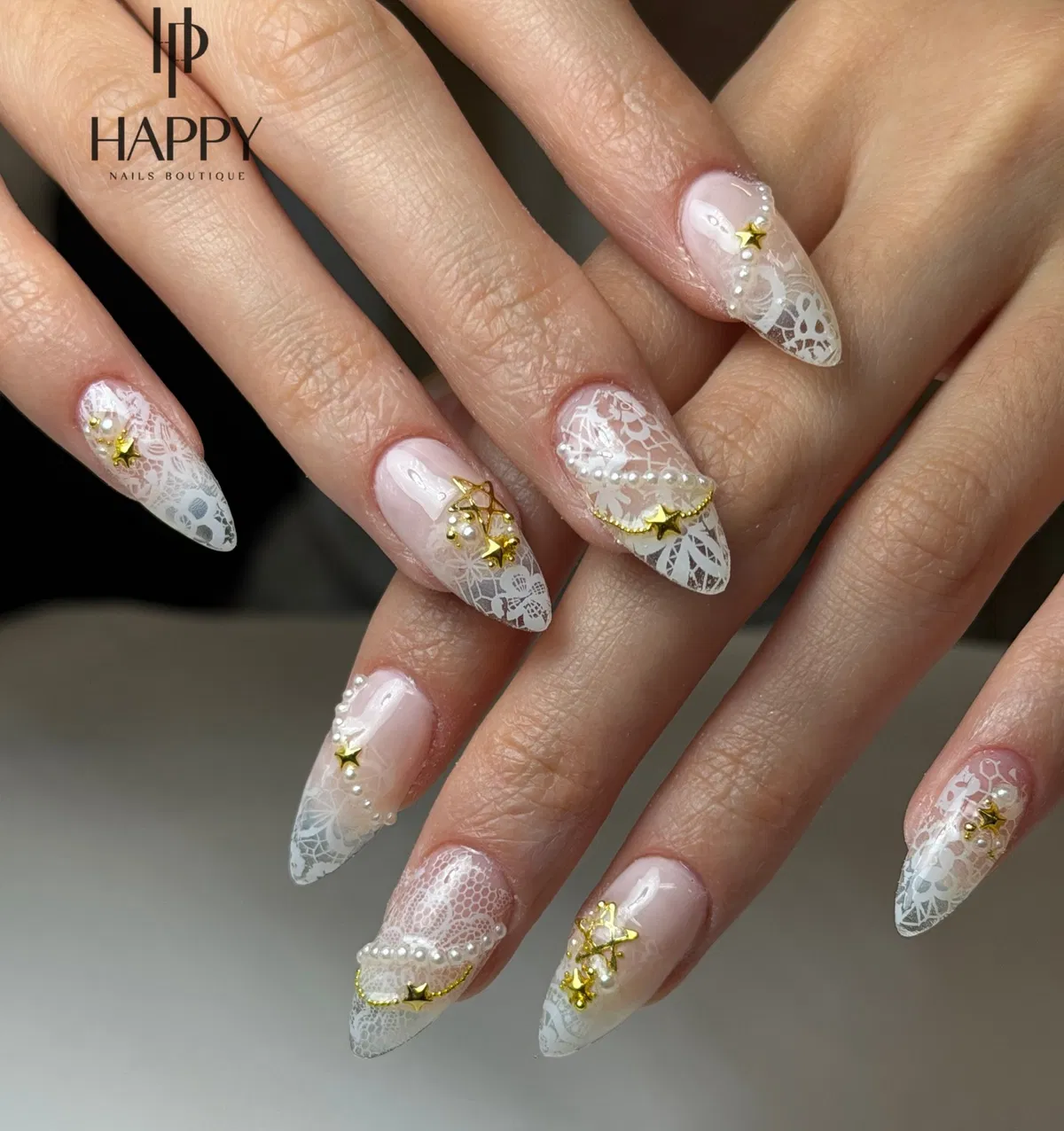 Stiletto nude-pink nails with white lace pattern, gold stars, and pearl accents