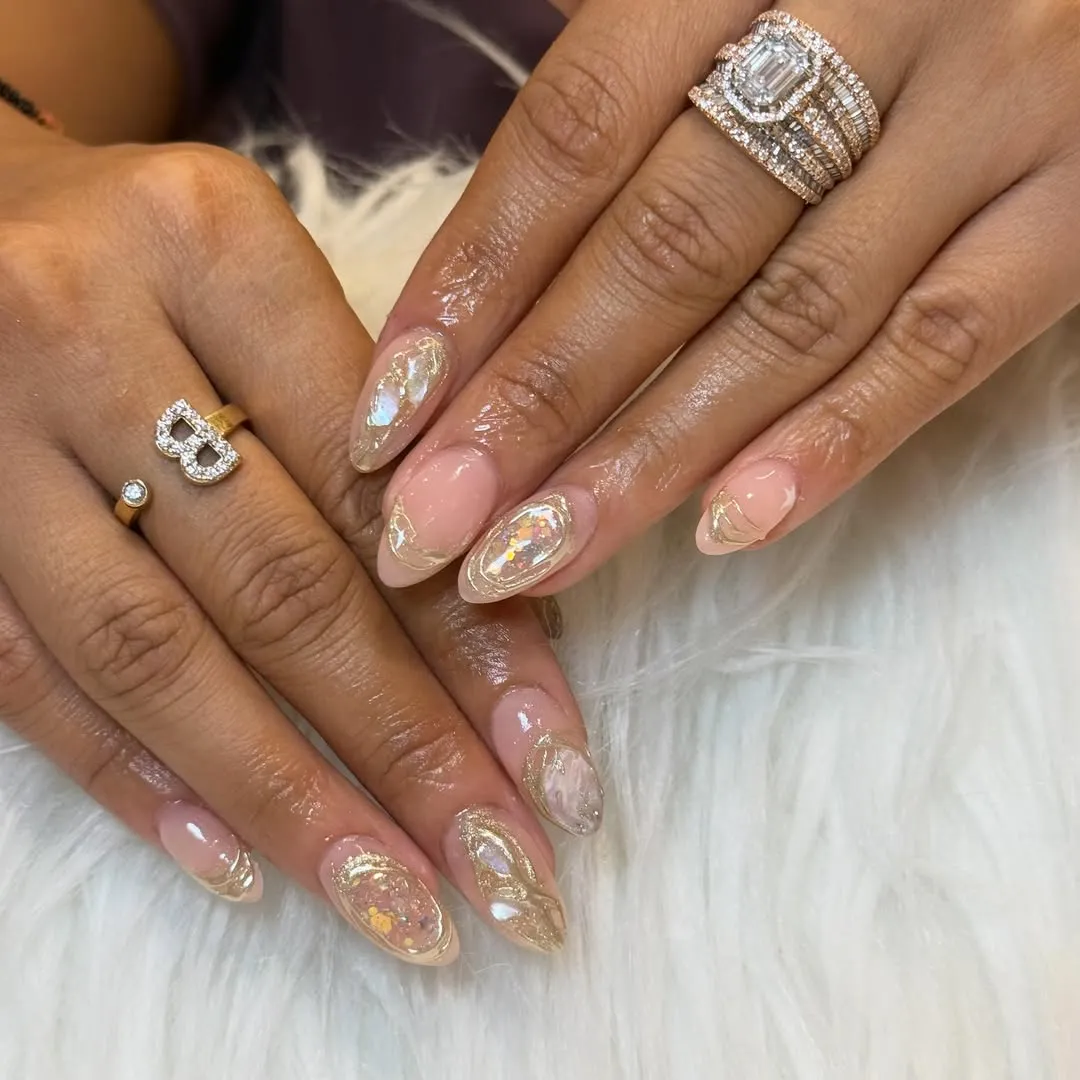 Sheer nude-pink almond nails with gold accents and iridescent flakes