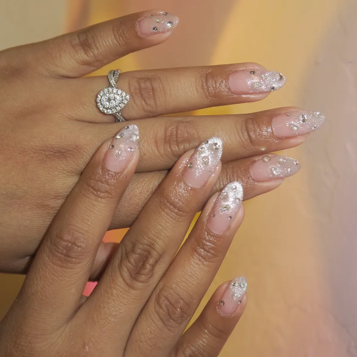 Nude-pink almond nails with silver glitter fade and scattered rhinestones
