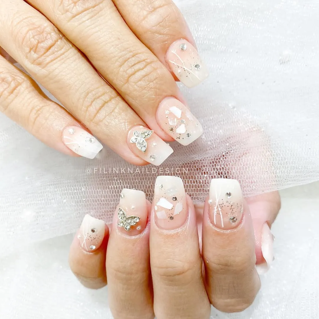 Nude-to-white ombré square nails with butterfly rhinestones