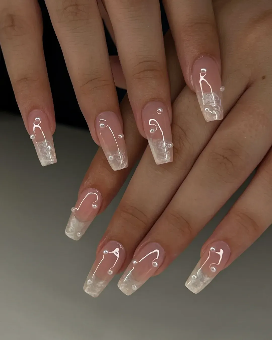Pink-to-white marbled tips with white swirl lines and pearl-like accents