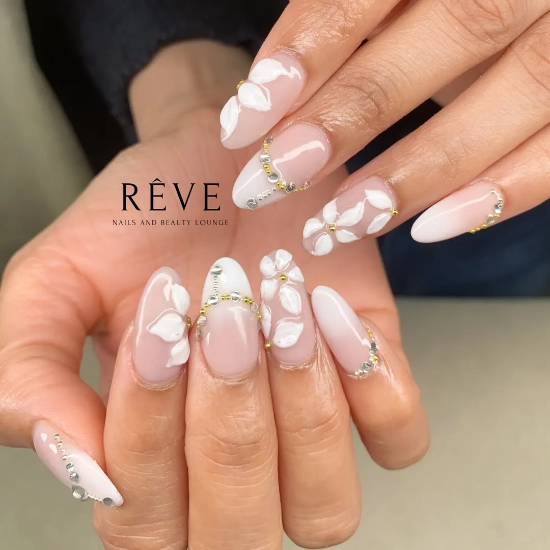 Long nude-pink nails with 3D white petals and beaded rhinestone curves