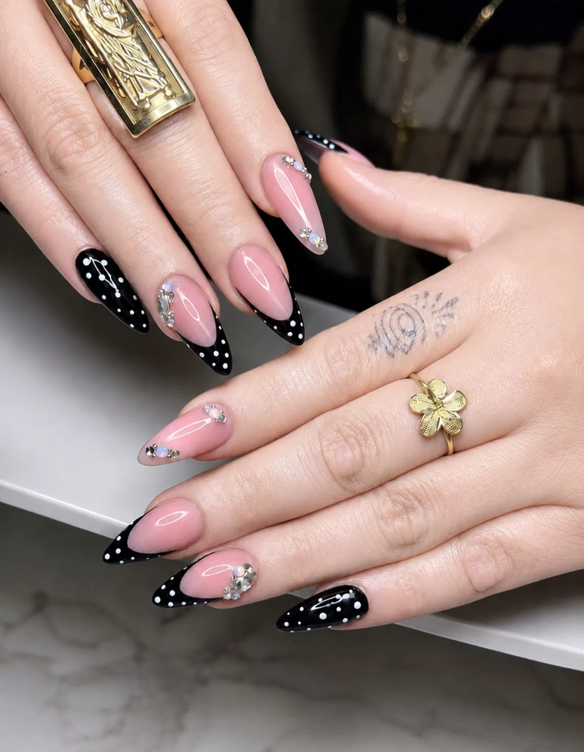 Almond nude nails with polka dot black tips and rhinestone accents