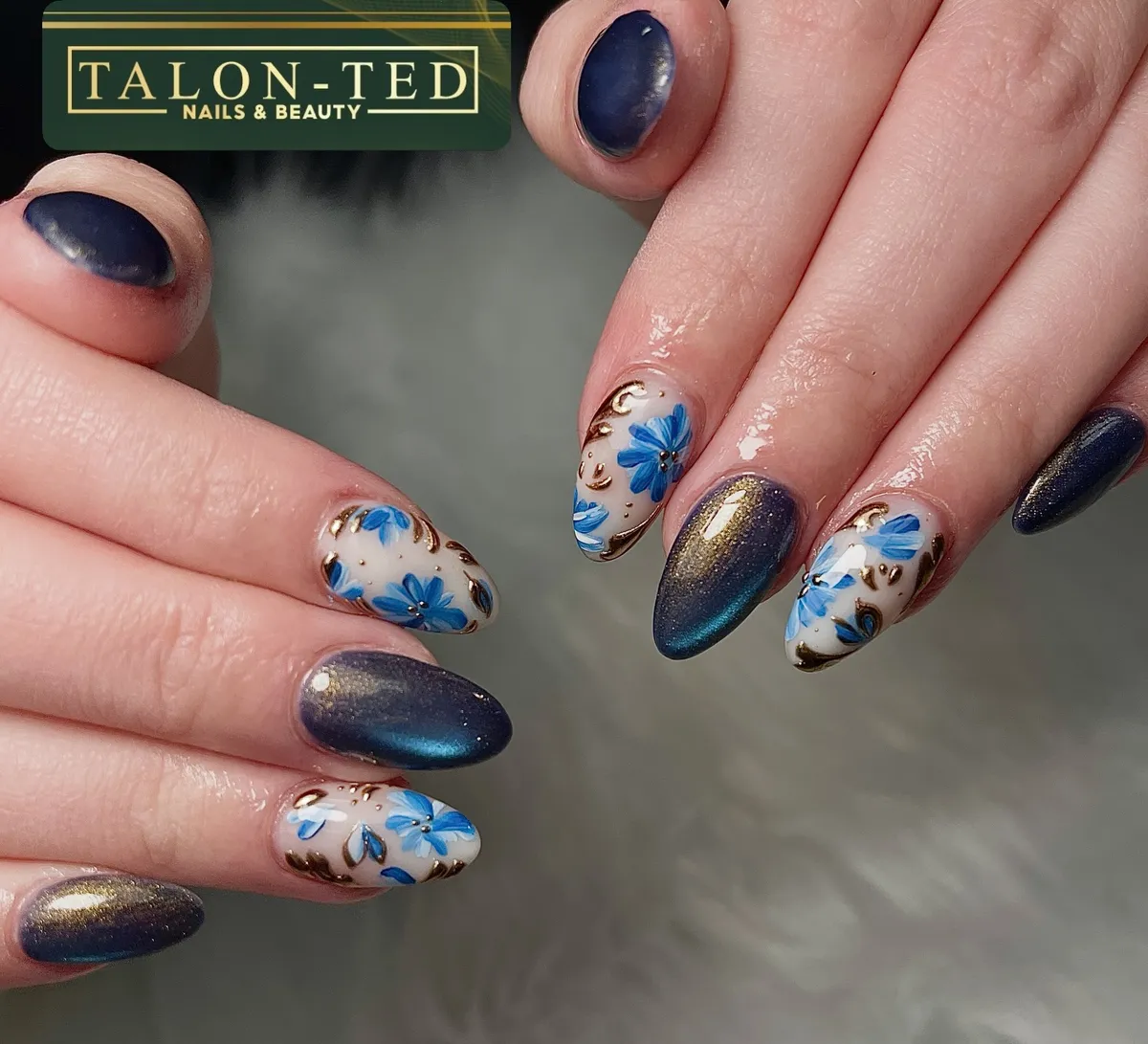 Metallic dark nails with blue florals and gold-toned accents