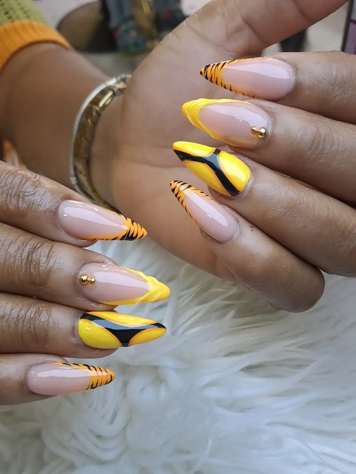Nude base with yellow tips, black striping, and gold studs