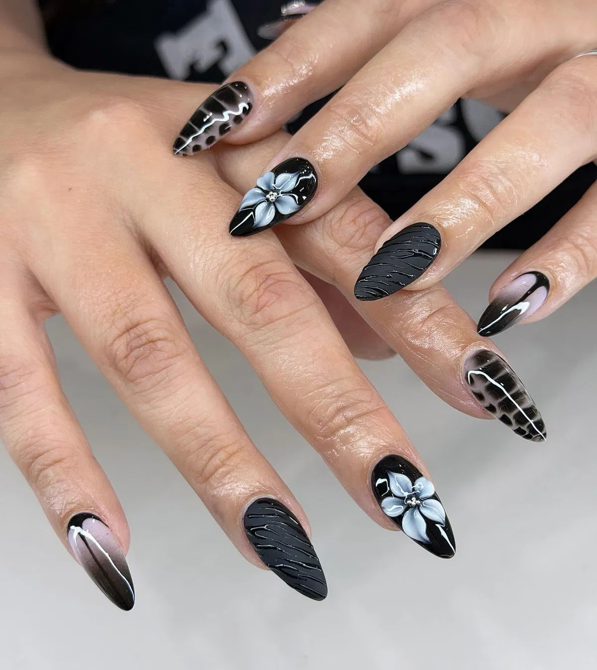 Glossy black almond nails with white stars and marbled accents