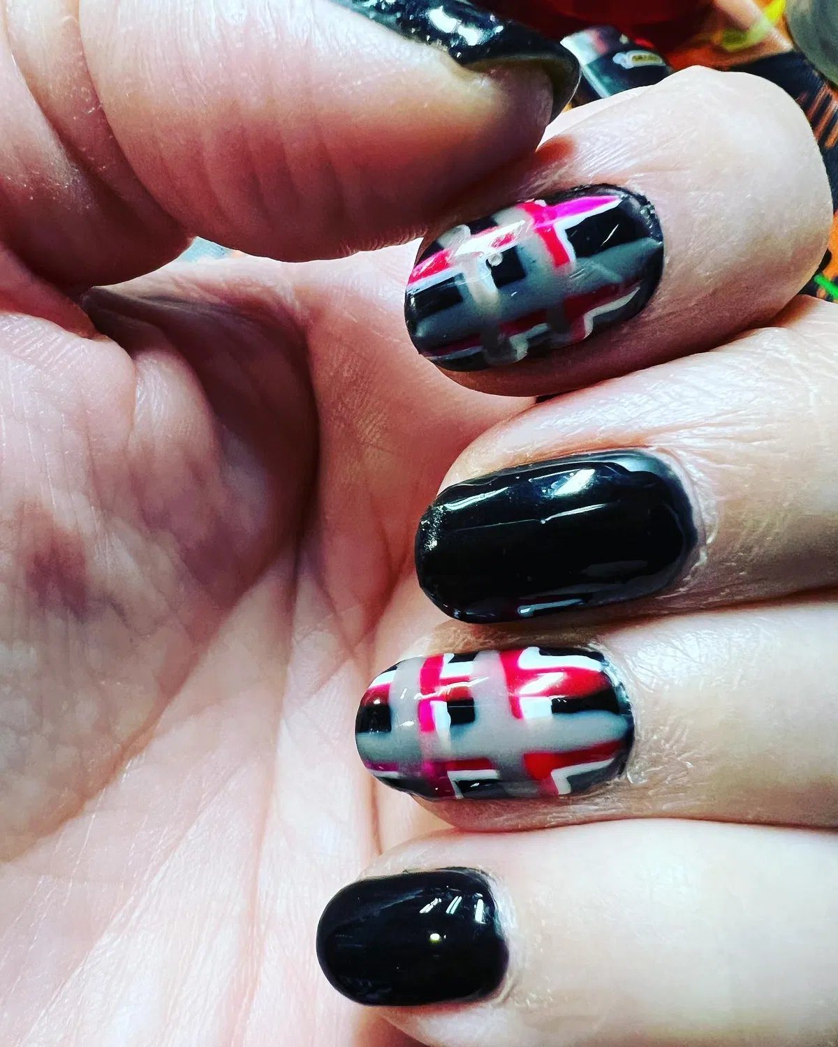 Glossy black nails with bold pink-and-gray plaid accents