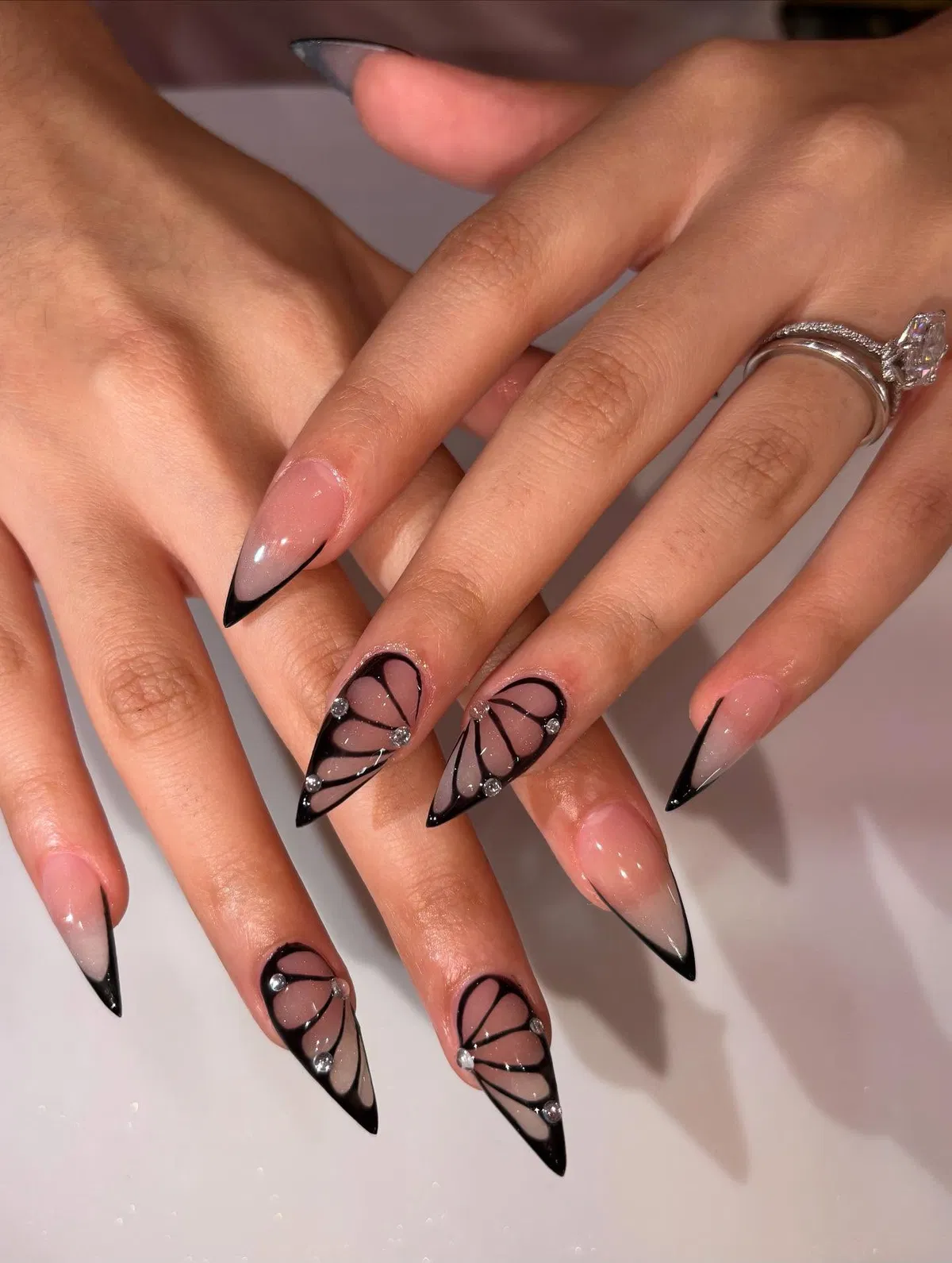 Thin black French tips with wing-like black linework and rhinestone accents