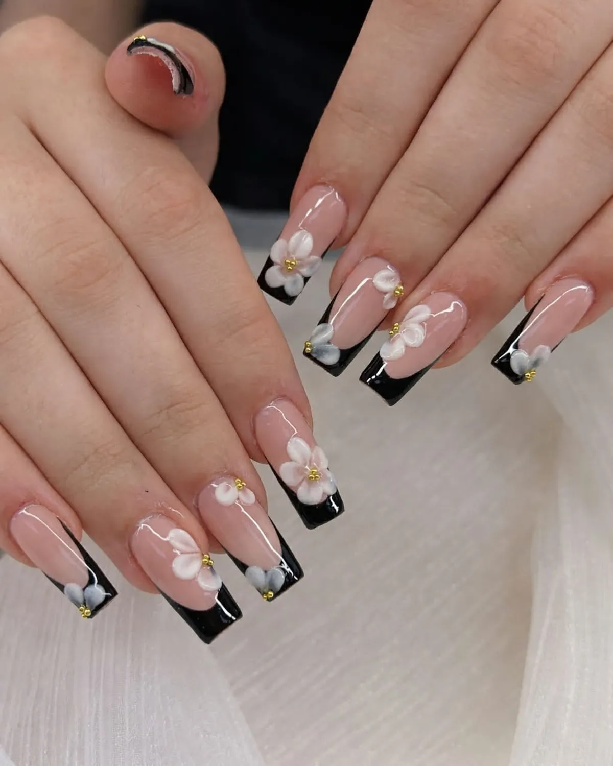 Square black French tips with white 3D flowers and gold bead centers