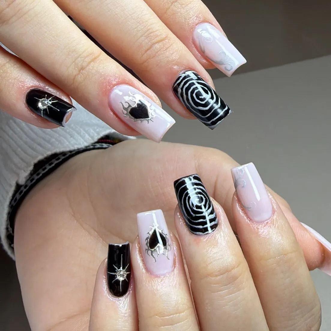 Pale pink and black square nails with spirals, hearts, and gem accents