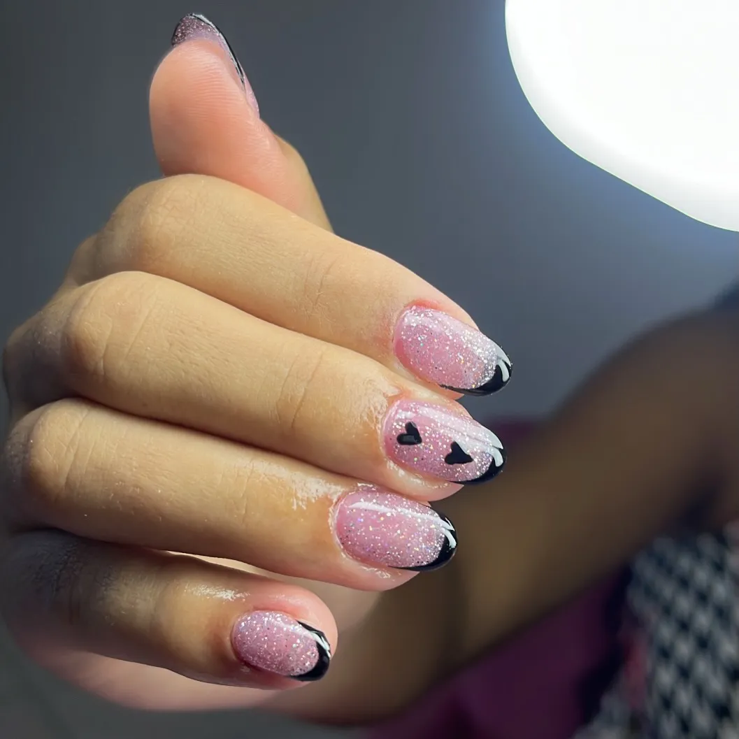 Pink shimmer almond nails with black tips and tiny hearts