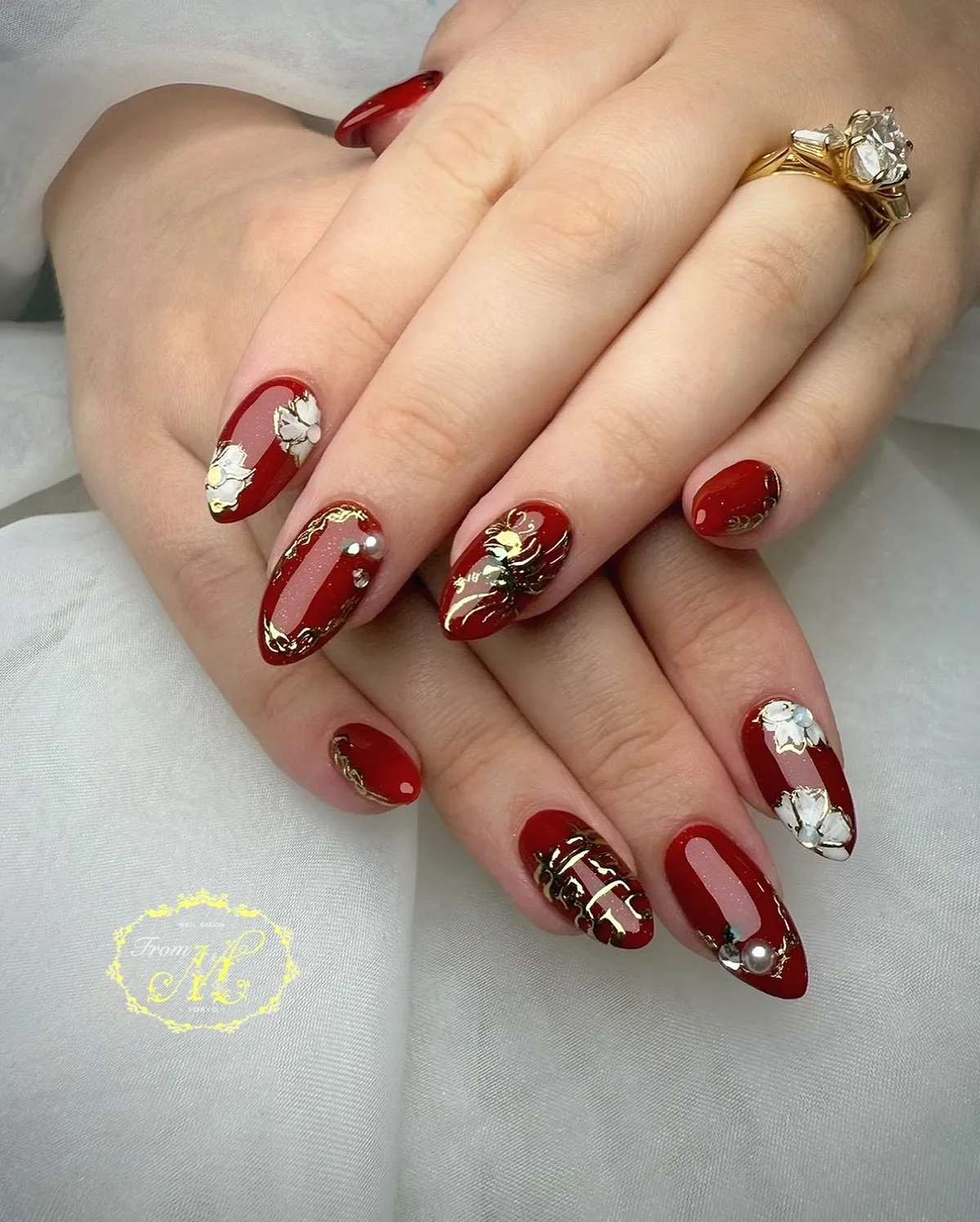 Red almond nails with gold detailing, flowers, and pearl accent