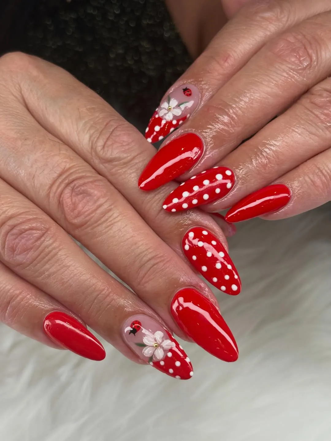 Red stiletto nails with polka dots, flowers, and ladybug accents