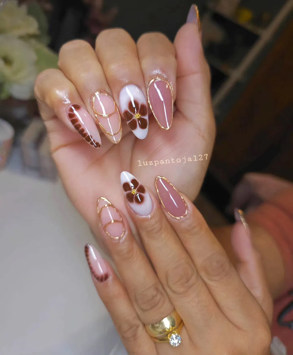 Gold-outlined almond nails with brown floral motifs