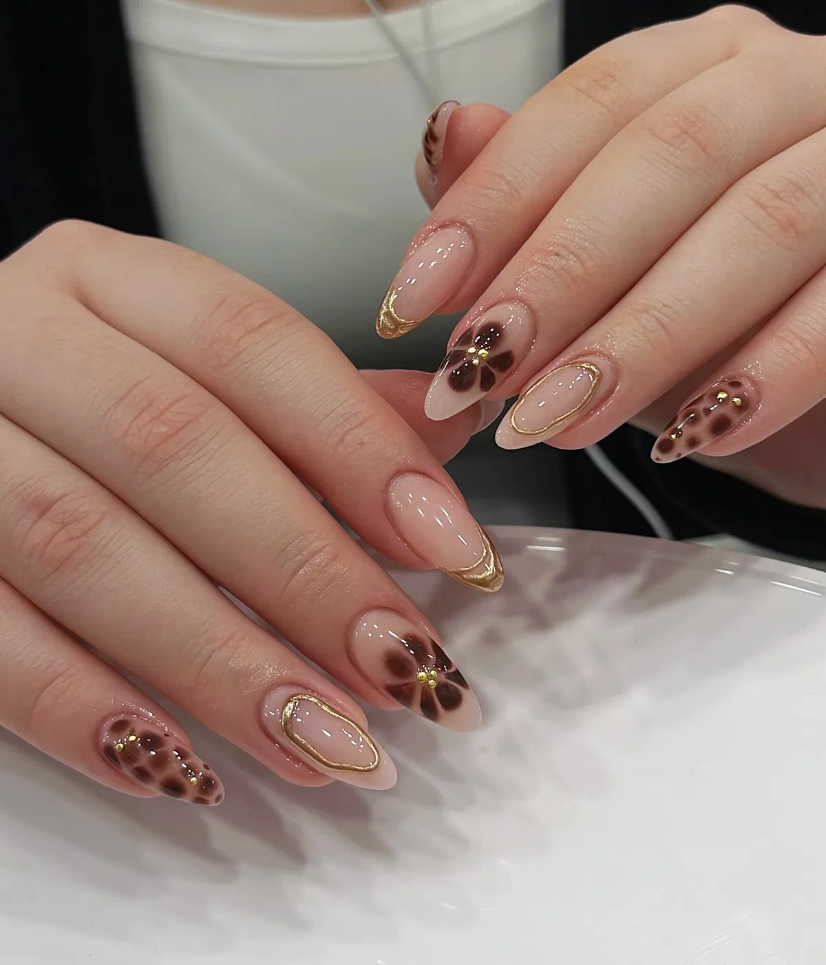 Nude almond nails with gold tips and brown floral accents