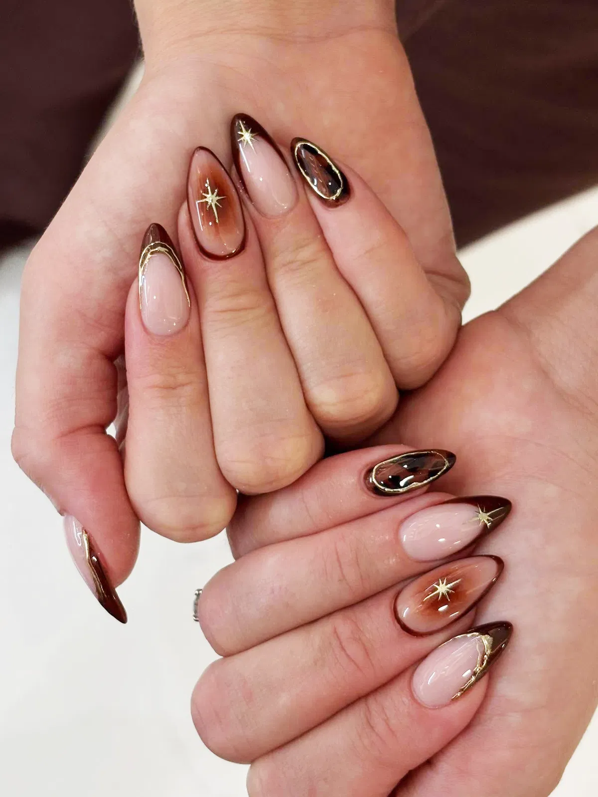 Brown-edged almond nails with gold starburst decals